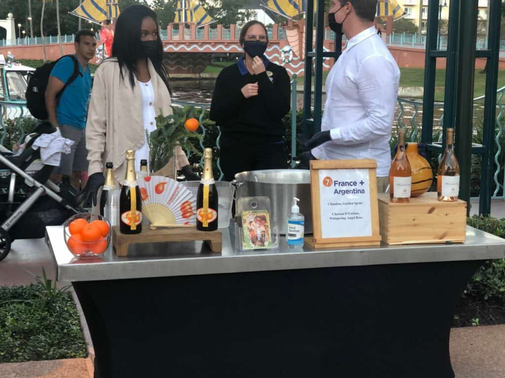 Guests mingle by a themed table featuring wine bottles, fresh oranges, and a France+Argentina sign at the Swan and Dolphin Food & Wine Classic at Walt Disney World.