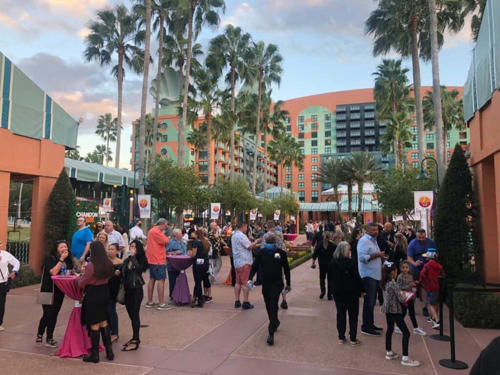 Guests mingle at cocktail tables outside the Swan and Dolphin resort, surrounded by palm trees and hotel towers, savoring the lively ambiance of Walt Disney World's celebrated Food & Wine Classic.