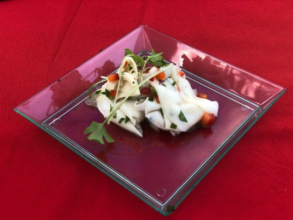 A fresh white noodle salad topped with colorful diced red peppers and herbs is served on a glass plate atop a red tablecloth, showcasing the lively flavors featured at the Food & Wine Classic inside Walt Disney World’s Swan and Dolphin Resort.