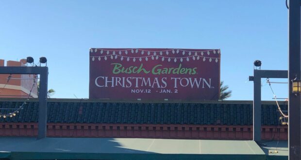 The Busch Gardens Christmas Town sign announces the festive event dates, Nov. 12 – Jan. 2, surrounded by sparkling string lights and holiday decorations, creating a warm holiday welcome for guests entering the park’s magical celebration.