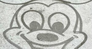 A playful sketch of Mickey Mouse’s face with oversized ears and a cheerful smile, created in water on the pavement—just like the spontaneous Water Art performances you spot throughout Walt Disney World.