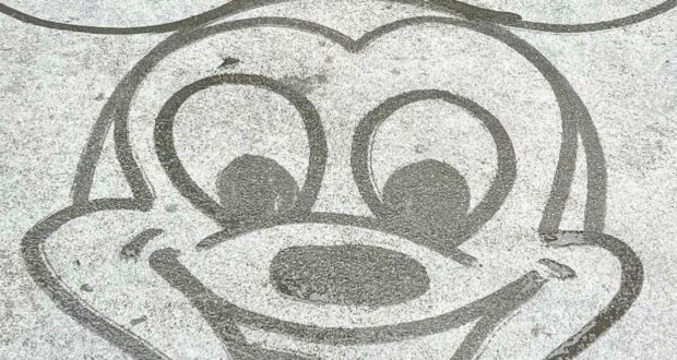 A playful sketch of Mickey Mouse’s face with oversized ears and a cheerful smile, created in water on the pavement—just like the spontaneous Water Art performances you spot throughout Walt Disney World.