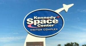 Kennedy Space Center Visitor Complex entrance sign featuring a rocket, set against a bright blue sky, promotes special Free Admission for Veterans to enjoy the space-themed attractions.