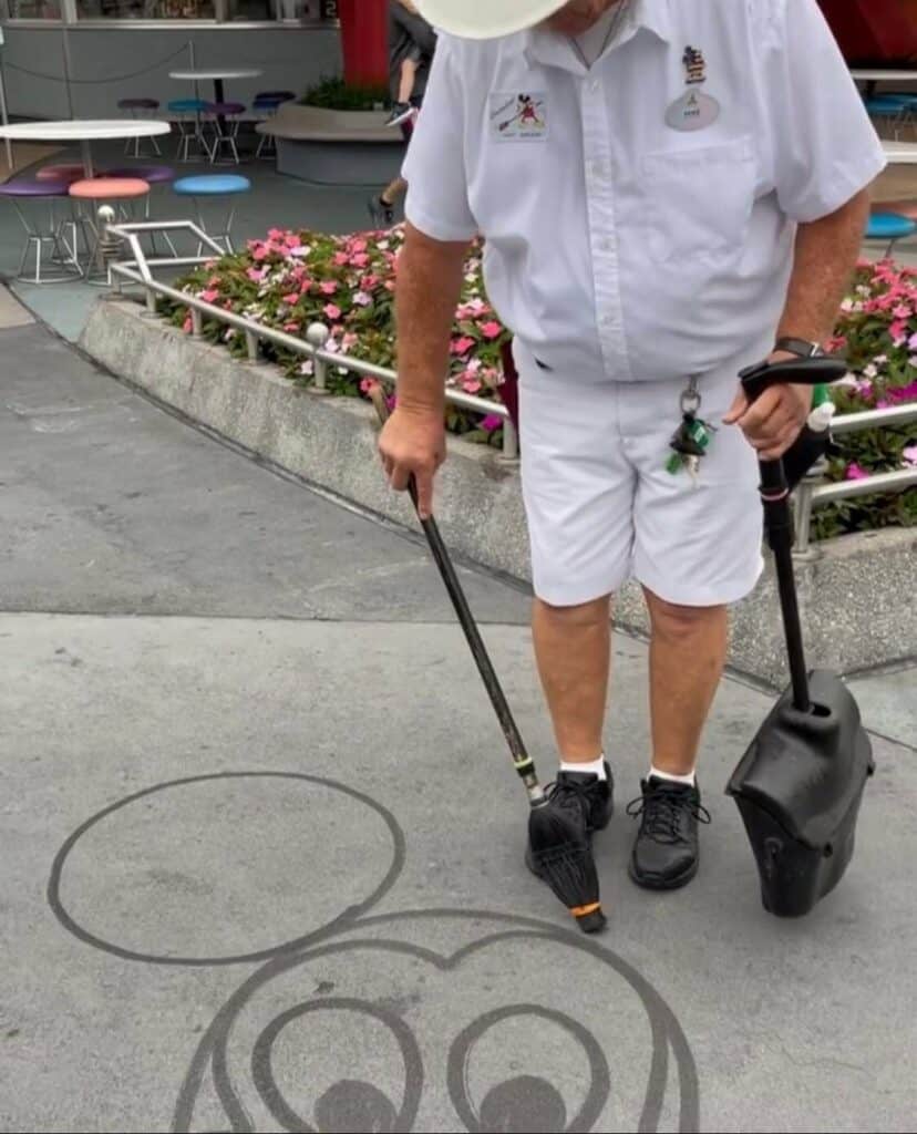 Mickey Mouse comes to life in magical Water Art, painted with a brush on the pavement at Walt Disney World, surrounded by vibrant blooming flowers.