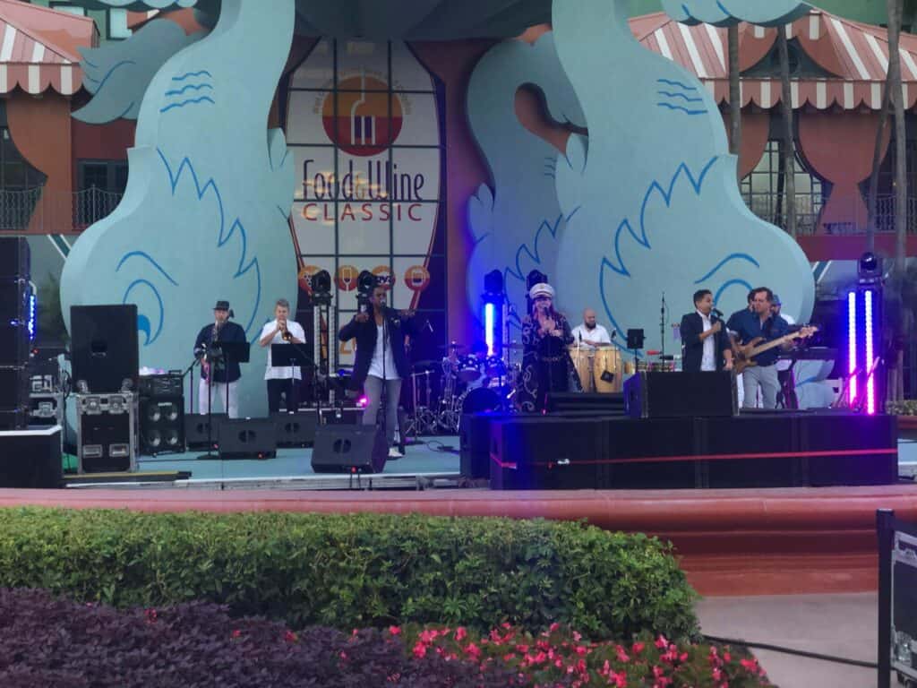 A lively band energizes the stage at Walt Disney World’s Food & Wine Classic at the Swan and Dolphin, filling the outdoor festival with music as guests savor gourmet dishes and world-class wines amidst the excitement of this renowned Disney celebration.