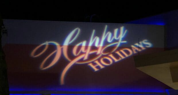 “Happy Holidays” lights up the night in festive script and block letters across a building at Magic Kingdom, adding extra sparkle to the Disney Very Merriest After Hours—an ideal spot to indulge in holiday treats and shop exclusive seasonal merch.