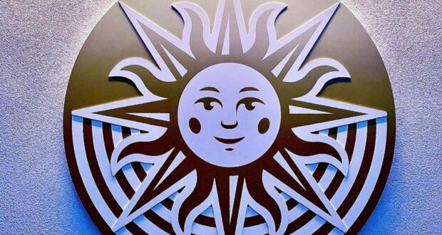 The iconic smiling sun from Drawn to Life beams with playful rays across a vibrant, patterned backdrop, radiating the cheerful energy and whimsical spirit that guests love in themed attractions.