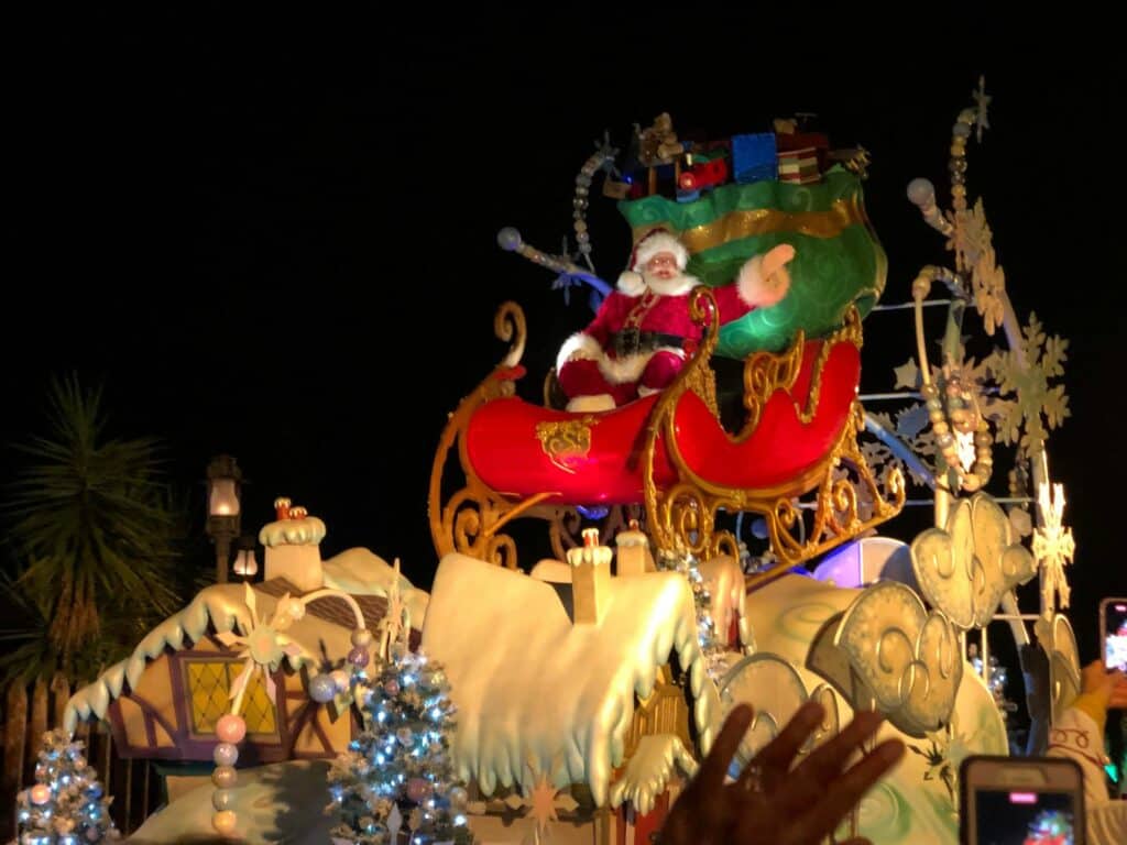 Santa Claus waves enthusiastically from his dazzling sleigh float, sparkling with holiday lights, snow effects, and gift-wrapped presents as he glides down Main Street during the magical Disney Very Merriest After Hours nighttime parade.