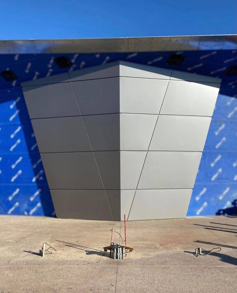 A sleek gray metal construction wall with sharp, angular panels stands in front of a blue building still under construction, channeling the adventurous style found near Guardians of the Galaxy: Cosmic Rewind at EPCOT.