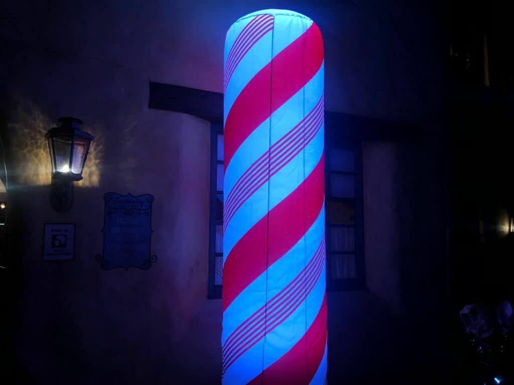 A glowing red, white, and blue barber pole shines brightly against the night, capturing the festive Disney Very Merriest After Hours vibe that lights up Magic Kingdom.