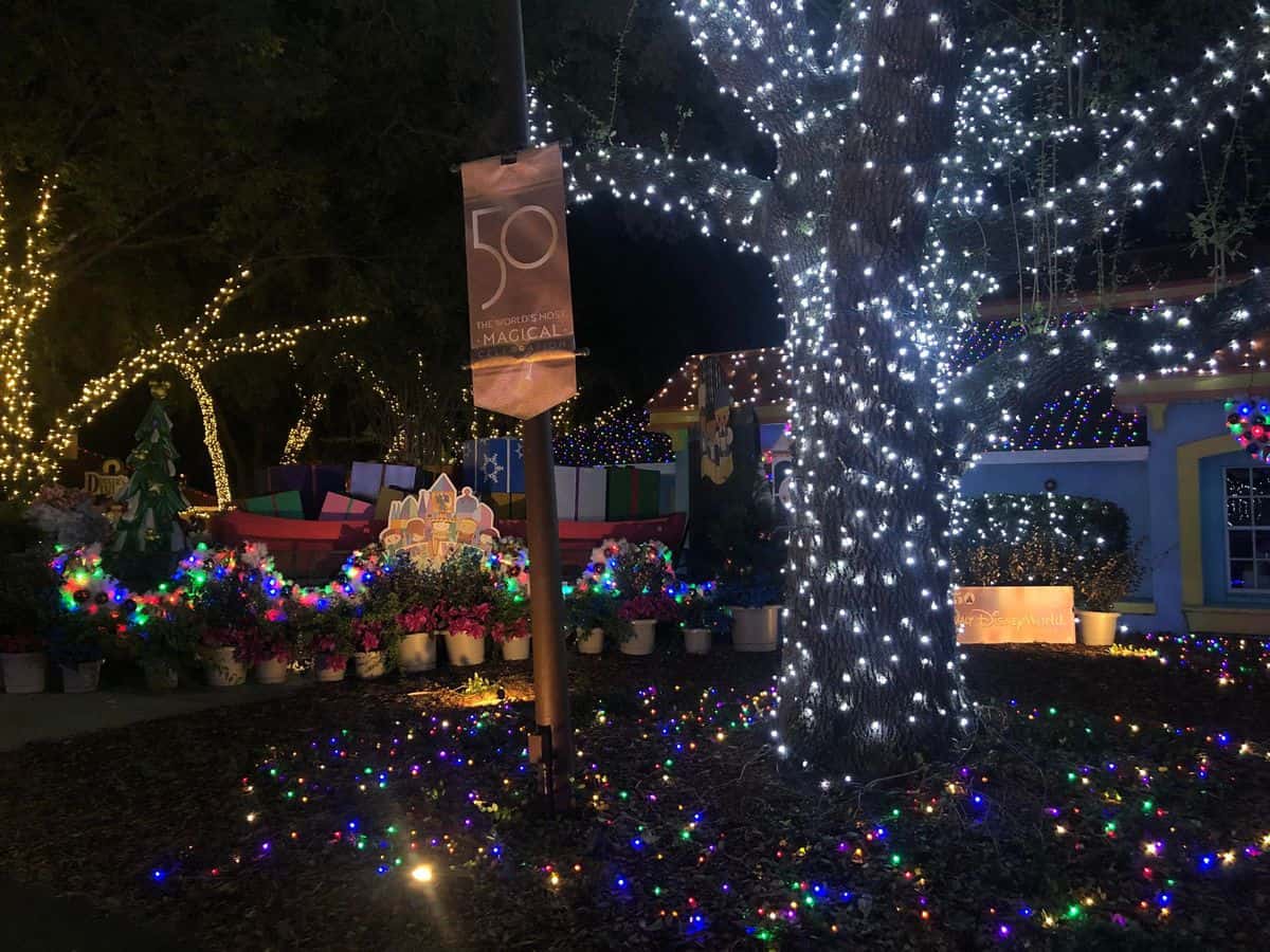 A festive scene at Give Kids the World’s Night of a Million Lights, featuring a house and towering tree dazzling with vibrant holiday lights, highlighted by a sparkling “50 Years Magical” banner celebrating the legacy of Walt Disney World Resort.