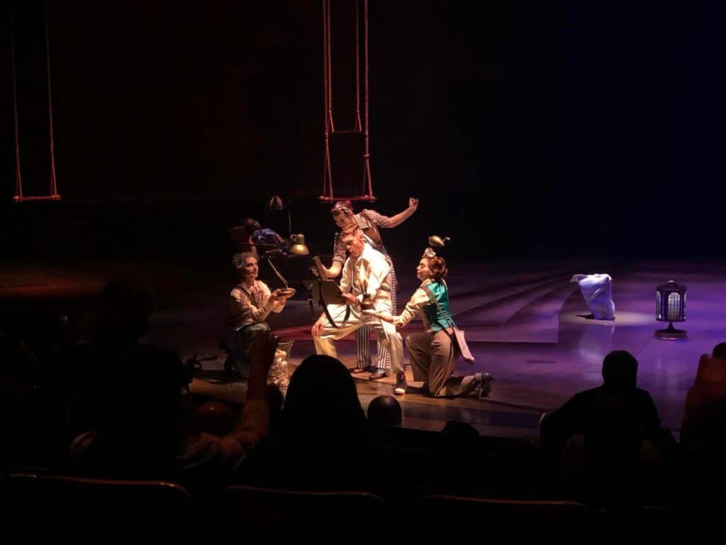 During opening night of Cirque du Soleil’s Drawn to Life, four colorfully costumed performers kneel and make expressive gestures on the dimly lit Disney Springs stage, captivating the audience with their theatrical performance.