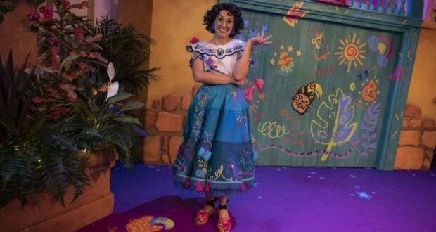 Mirabel beams in a colorful outfit, striking a playful pose amid lush plants and an enchanting, vibrant backdrop inspired by the world of Encanto at Disney California Adventure Park.