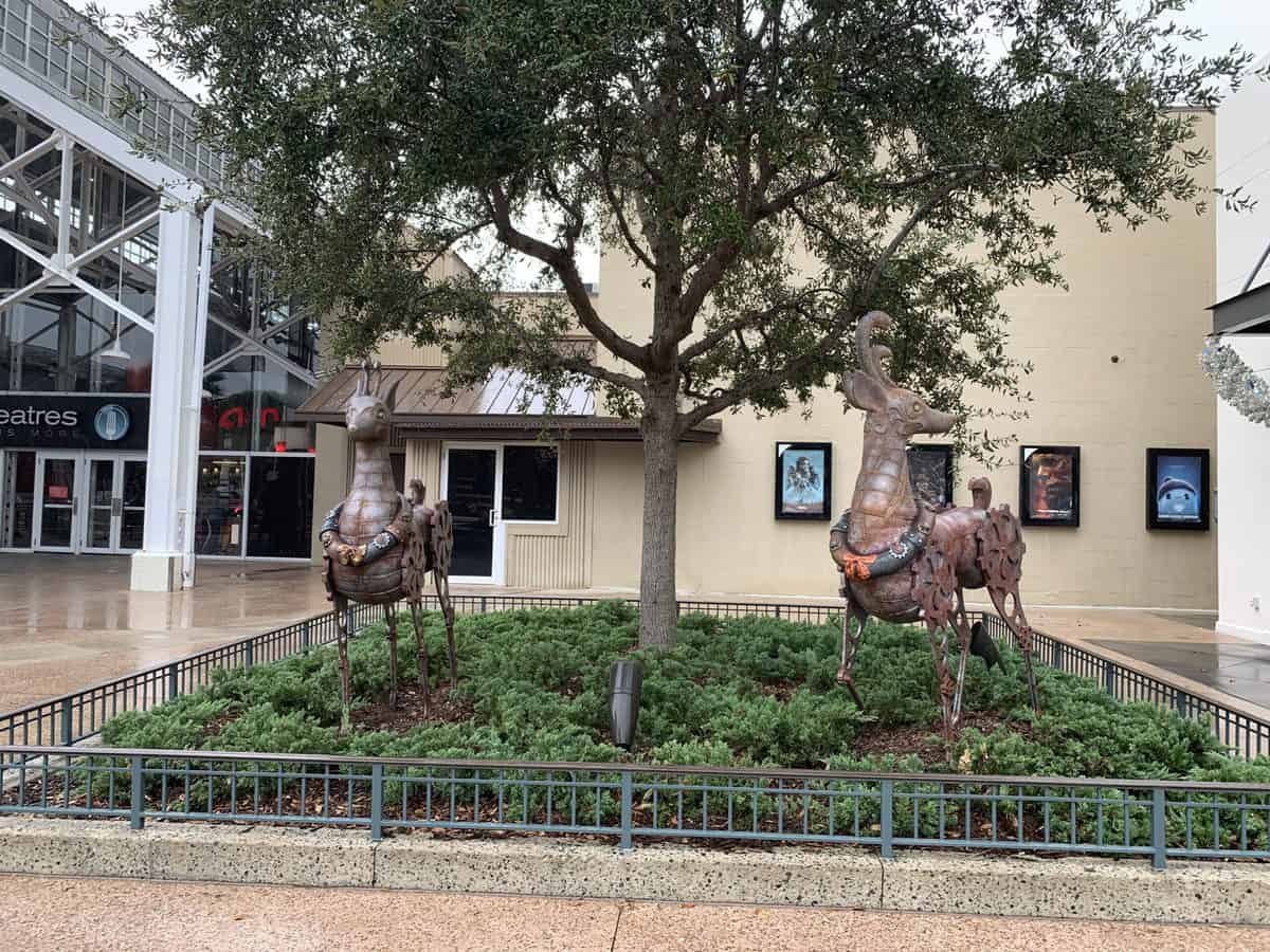 Three whimsical bronze horse sculptures greet guests beneath a tree in a cozy, fenced garden just outside the movie theater at the entertainment complex, adding festive cheer for families and fans exploring the park’s 2021 Christmas celebration and holiday stroll.