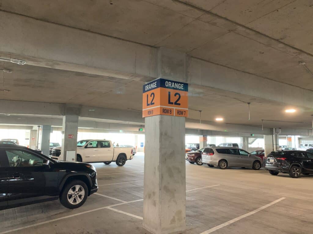 Disney Springs parking garage with cars and a clearly marked column reading "Orange L2, Row 8, Row 7" beneath a concrete ceiling, making it easy for guests to remember their spot and find their way back after shopping, dining, or enjoying entertainment at Disney Springs.