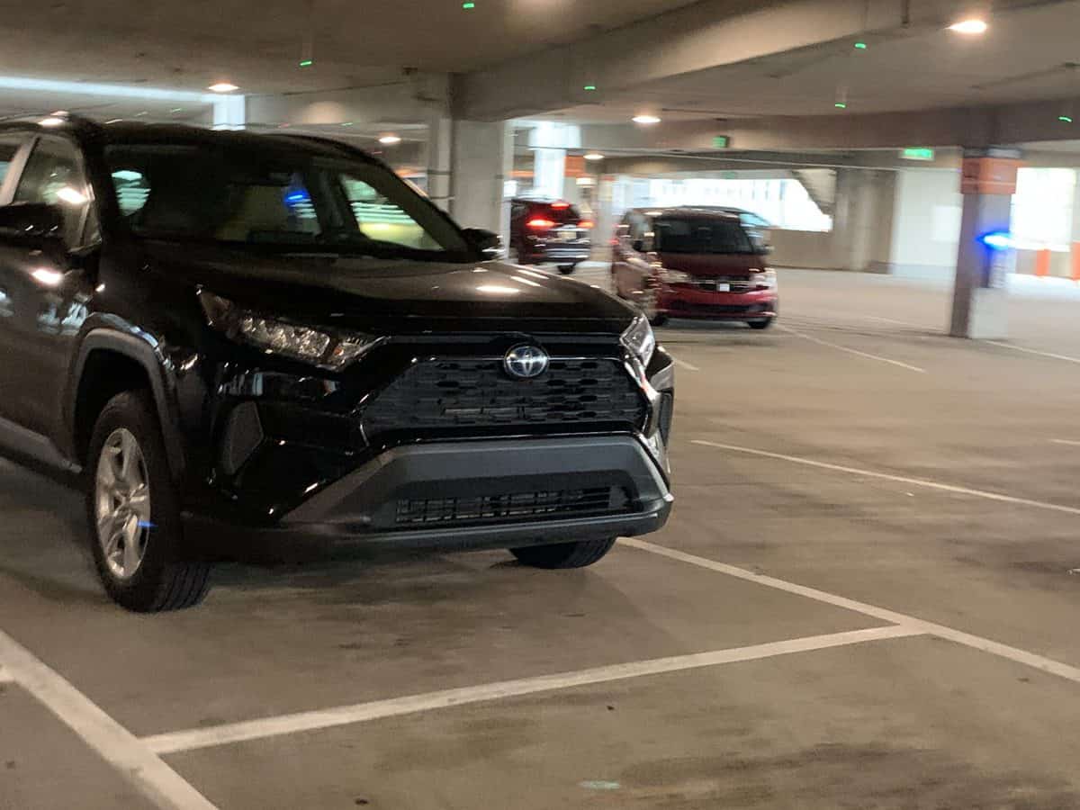 A black Toyota SUV is parked inside a multi-level Disney Springs parking garage, with a red car visible in the background—showcasing premier parking just steps away from all the shops, dining, and excitement of Disney Springs.