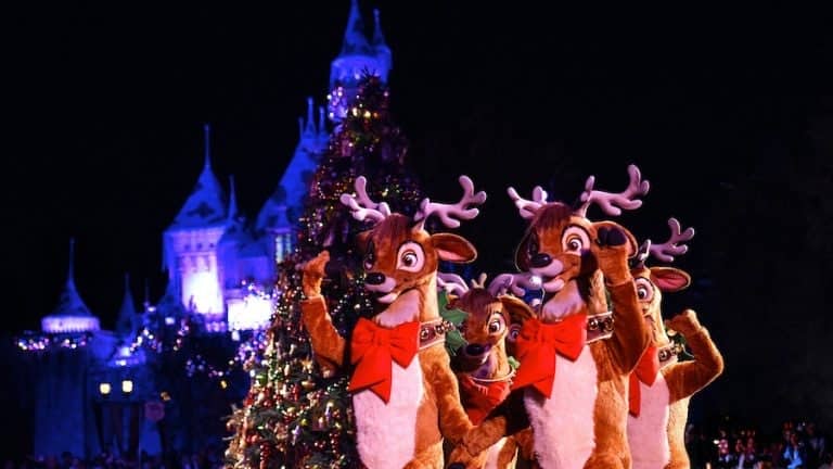 Reindeer dancers parade past a sparkling Christmas tree beneath the dazzling lights of Disneyland’s iconic It’s a Small World facade, creating festive holiday magic after dark.