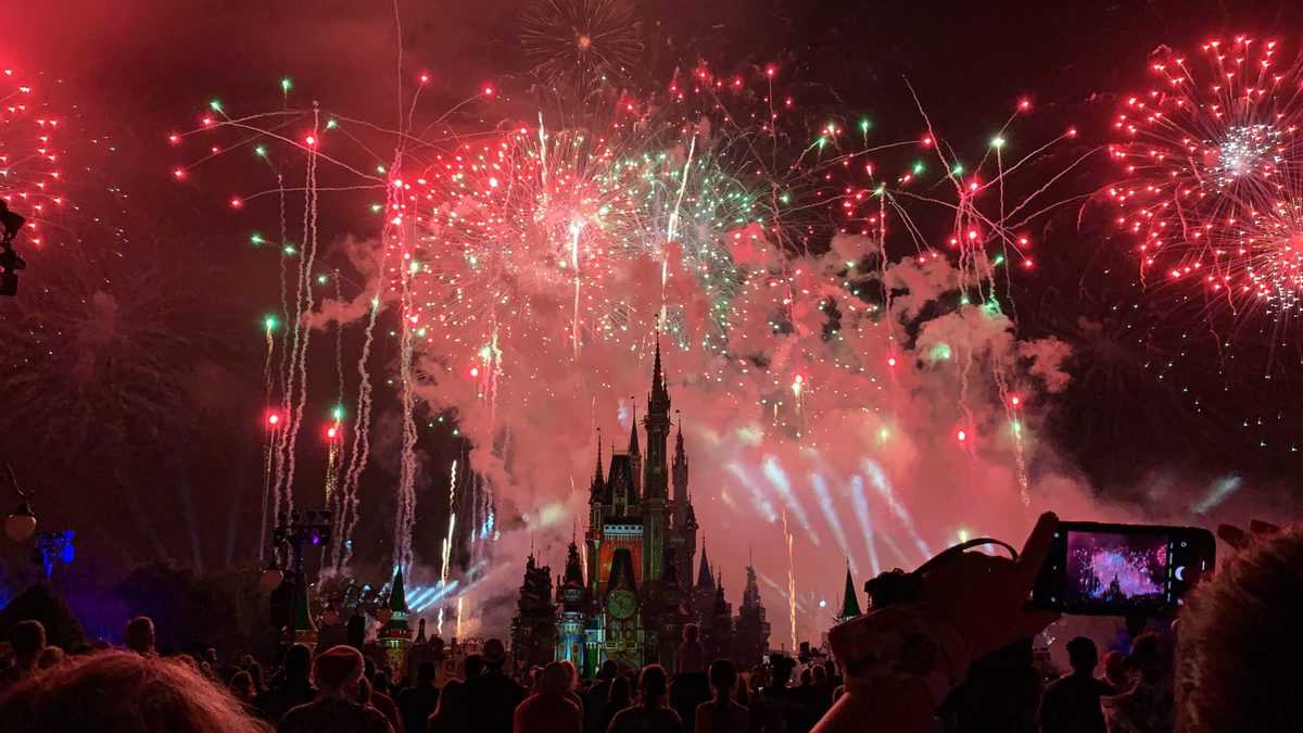 Red and green fireworks burst above Cinderella Castle at night as Disney fans gather below, some snapping photos to remember the magical atmosphere of Very Merriest After Hours.