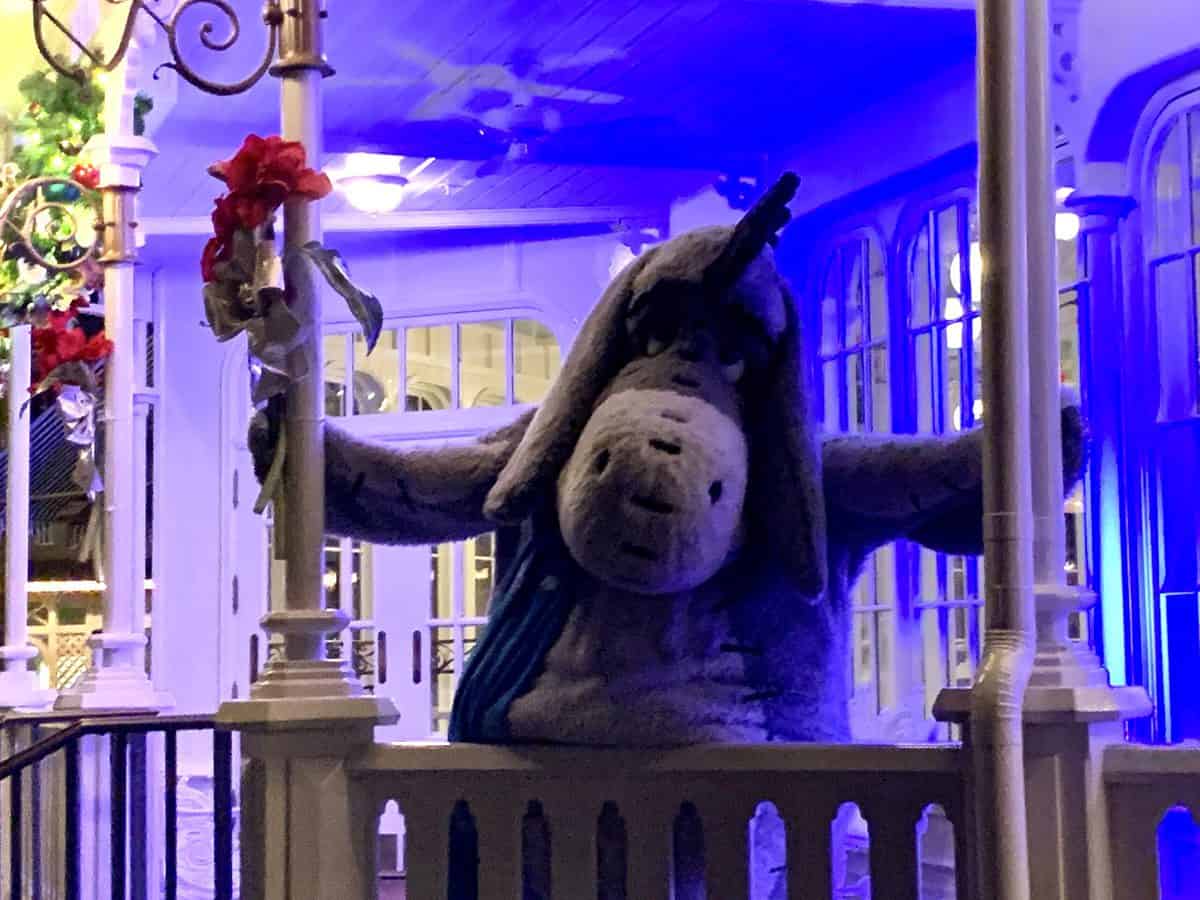 Eeyore greets guests with arms outstretched on a flower-adorned porch under the night sky, bringing Disney Very Merriest After Hours magic to life.