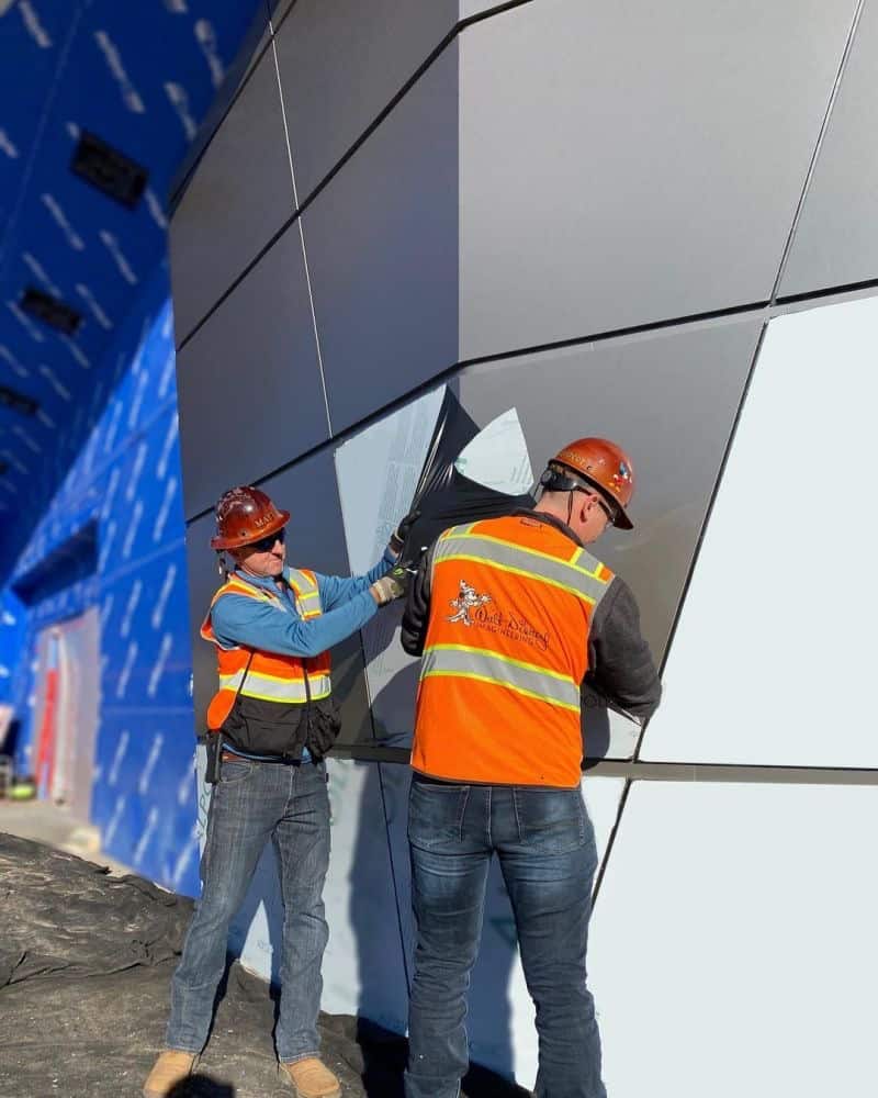 Crew members in safety vests and helmets work on installing massive gray panels to the exterior of Guardians of the Galaxy: Cosmic Rewind, showcasing thrilling construction progress at EPCOT.