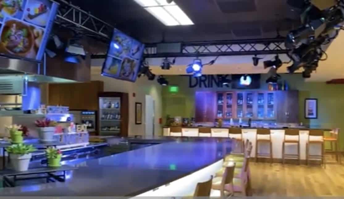 The Flavor Lab’s dazzling TV studio kitchen, featuring sleek cooking stations, lively bar seating, vibrant lighting, and dynamic food images on high-def monitors—an immersive setting where Universal Orlando’s culinary team wows guests during interactive demos or backstage experiences that reveal the magic behind Universal’s signature dishes.