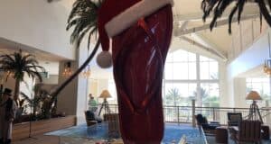 A towering red flip-flop decked with a Santa hat takes center stage in the lively, festive lobby of a tropical resort, surrounded by colorful holiday ornaments—a holiday display that brings beach vibes to your sunny getaway.