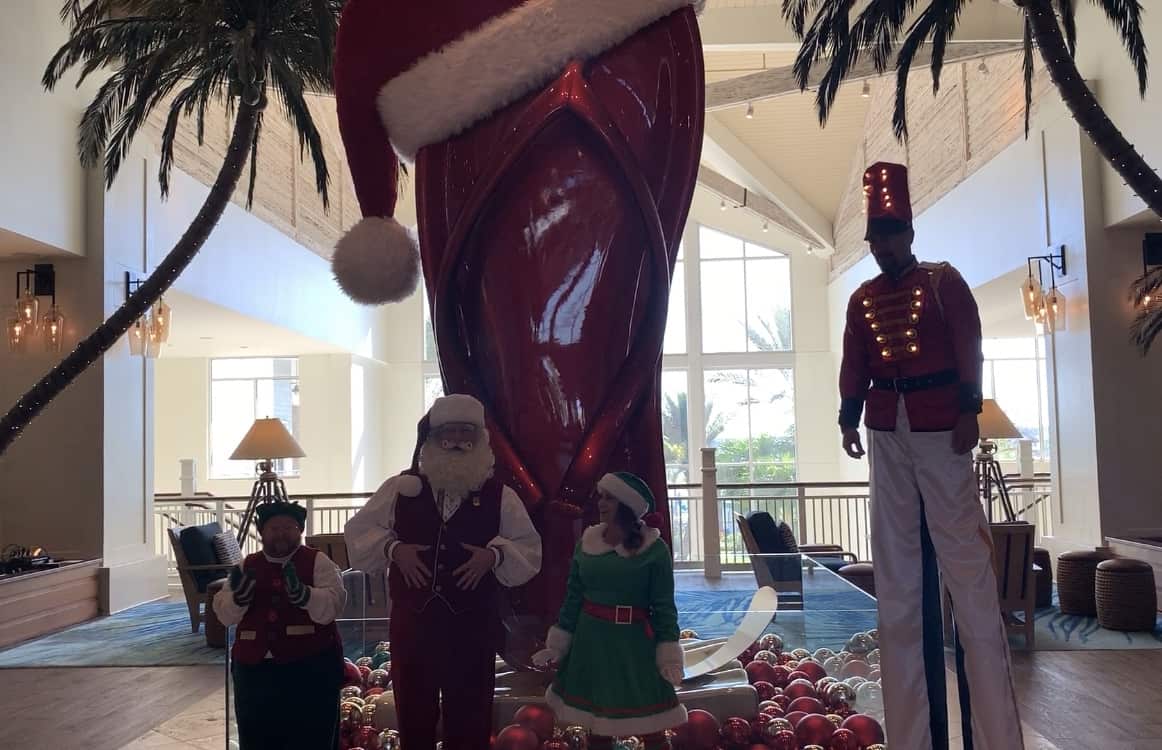 Holiday revelers in cheerful Christmas costumes pose amid oversized red ornaments and festive decor in the lively Margaritaville Resort Orlando lobby, capturing the holiday spirit just steps from all the excitement of Orlando’s world-famous theme parks.