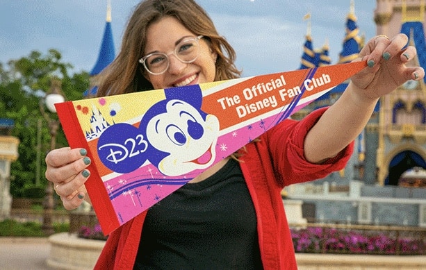 A Disney fan beams as she waves a vibrant D23 Fan Club pennant in front of Cinderella Castle at Walt Disney World, proudly celebrating her new D23 Gold Duo Membership—unlocking 50% off exclusive Disney experiences.