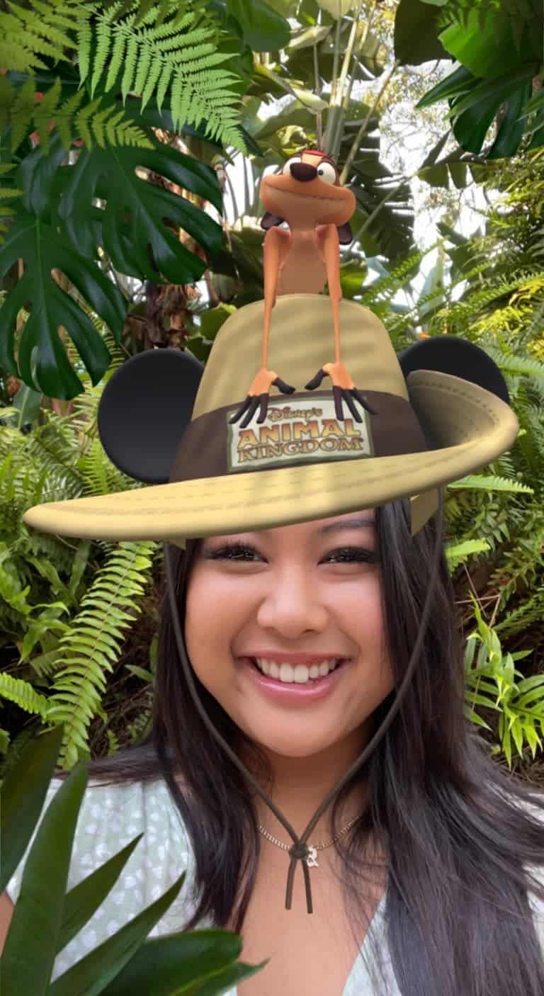 Disney fan smiling in a lush, adventure-themed backdrop, sporting a playful safari hat filter topped with a cartoon bird—radiating excitement to share top Genie+ strategies and insider tips for unlocking every magical Disney moment.