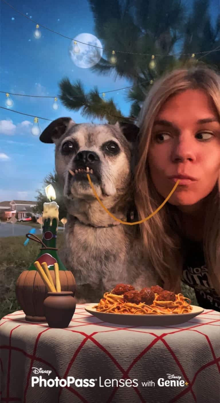 A woman and her dog share a single spaghetti strand at a candlelit patio table, recreating the iconic Lady and the Tramp moment in true Disney style—capturing the heartwarming romance that Disney fans love, just like discovering Genie+ and unlocking magical new experiences throughout Walt Disney World.