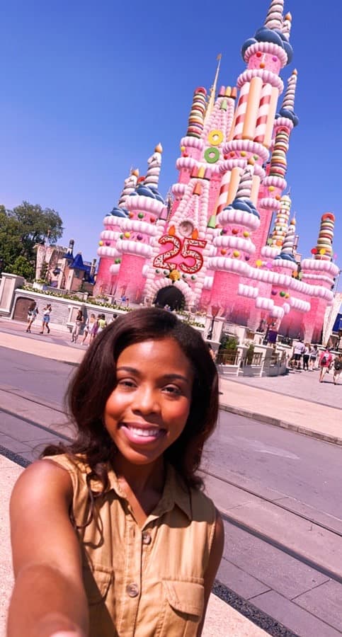 Guest snapping a selfie in front of Magic Kingdom’s vibrant, cake-themed Cinderella Castle during Disney World’s 25th Anniversary celebration, making the most of the magic with insider park tips and Disney Genie+.