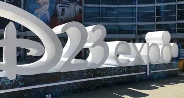 The bold white "D23 Expo" sign stands outside the convention center, with Elsa from Frozen and Baymax from Big Hero 6 featured on vibrant posters behind it, greeting Disney fans as they arrive for the excitement of Destination D23.