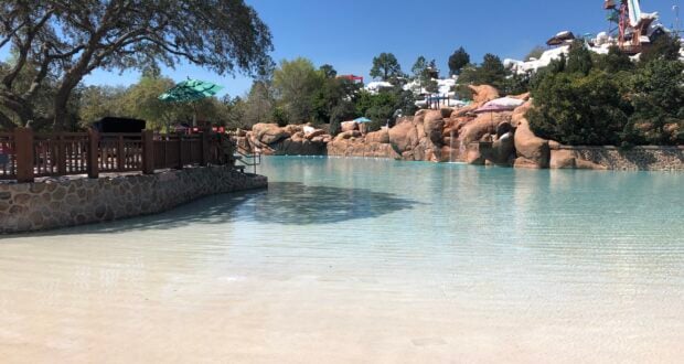 Blizzard Beach’s scenic, family-friendly pool welcomes guests with its tranquil, shallow waters set against a rugged mountain backdrop. The iconic wooden railings, lush trees, and thrilling water slides in the background invite you to relax and play in this celebrated Disney water park.