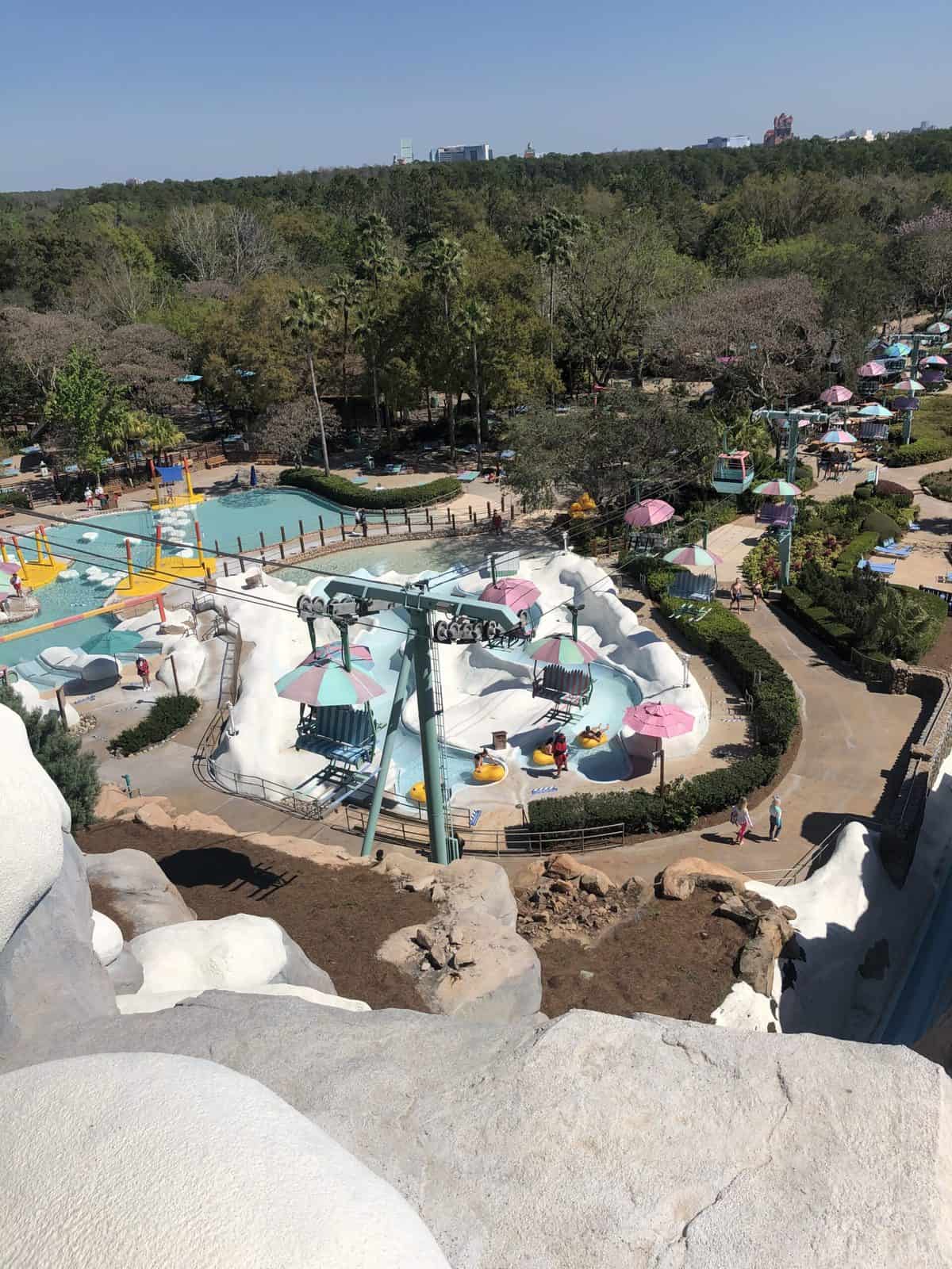 Aerial view of Disney’s Blizzard Beach featuring colorful pools, thrilling water slides, rows of sun umbrellas, and guests making the most of a sunny day at this iconic water park before closing time.