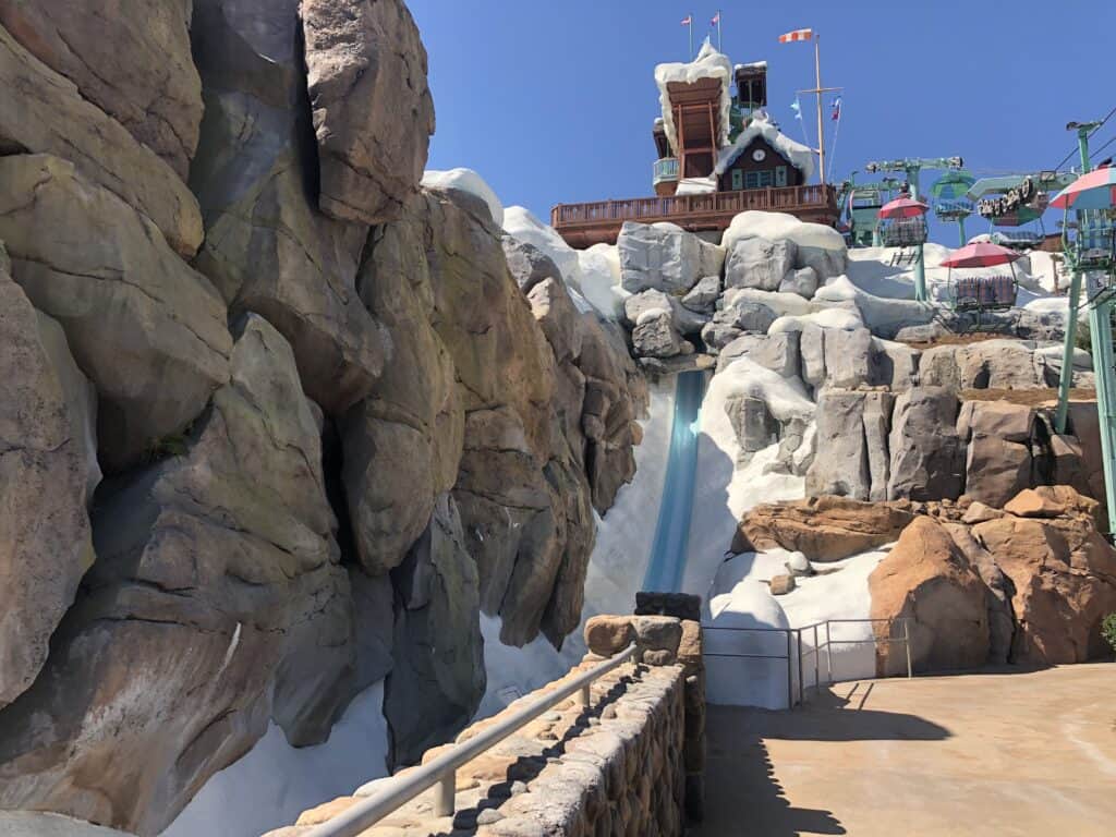 Summit Plummet, Blizzard Beach’s iconic waterslide, plunges dramatically between snowy, rock-lined cliffs beneath a bright blue sky at Disney’s newly reopened water park.