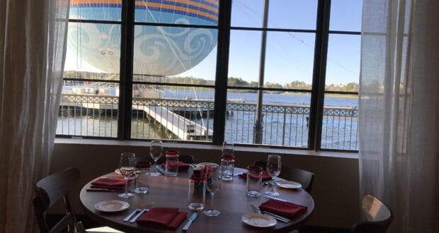 A beautifully arranged dining table set by the window overlooks shimmering water and a vibrant hot air balloon floating just outside, capturing the enchanting atmosphere of a Disney World holiday breakfast experience.