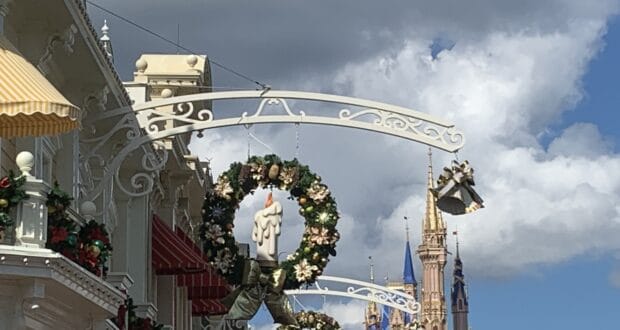 Main Street, U.S.A. in Magic Kingdom comes alive for the holidays with festive wreaths and glowing candle decorations, while Cinderella Castle shimmers in the background against a bright blue sky, immersing guests in Disney’s signature seasonal magic.