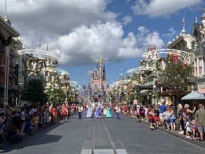 Main Street, U.S.A. bursts with holiday excitement at the Magic Kingdom, where a dazzling parade entertains joyful Disney fans and Cinderella Castle glows beneath clear blue skies in the festive atmosphere.