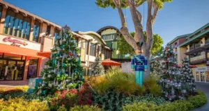 Whimsically decorated Christmas trees and a classic Toy Soldier statue create a lively, holiday-themed scene in an open-air shopping plaza, evoking the magical festivities of Main Street, U.S.A. at Disneyland.
