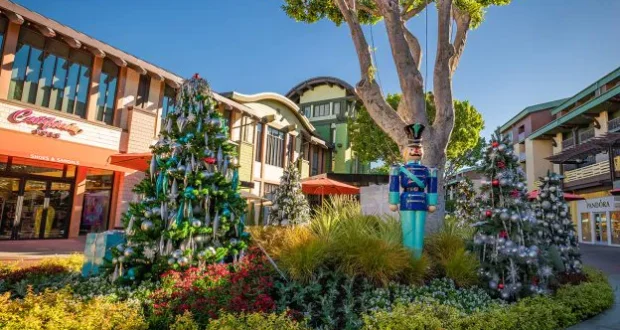 Whimsically decorated Christmas trees and a classic Toy Soldier statue create a lively, holiday-themed scene in an open-air shopping plaza, evoking the magical festivities of Main Street, U.S.A. at Disneyland.