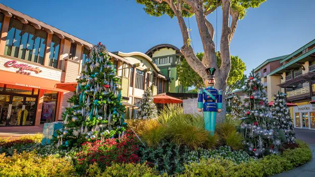 Whimsically decorated Christmas trees and a classic Toy Soldier statue create a lively, holiday-themed scene in an open-air shopping plaza, evoking the magical festivities of Main Street, U.S.A. at Disneyland.