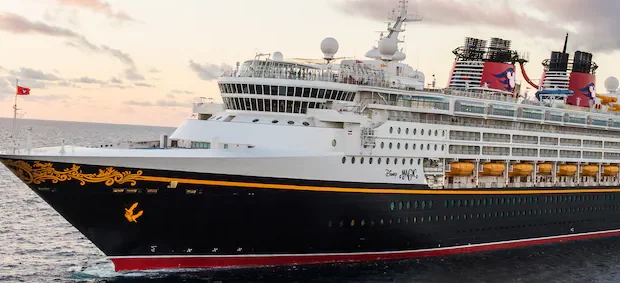 A majestic Disney Cruise Line ship glides across the ocean at sunset, set against a dramatic sky—inviting guests to experience up to 30% savings on their next magical Disney adventure at sea.