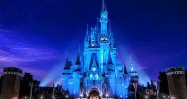 Cinderella Castle at Magic Kingdom shines with vibrant blue lights and towering spires against the night sky, with other beloved Disney icons aglow for Disney+ Day festivities.