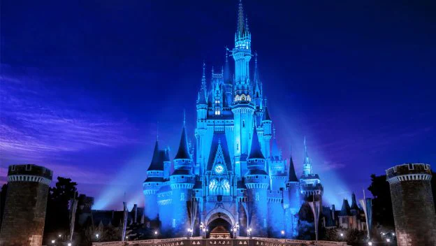 Cinderella Castle at Magic Kingdom shines with vibrant blue lights and towering spires against the night sky, with other beloved Disney icons aglow for Disney+ Day festivities.