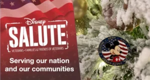Disney Salute banner displayed next to a snowy Christmas tree branch adorned with a Mickey Mouse military ornament, celebrating the holiday magic while recognizing Disney Salute Teams at Holidays at Walt Disney World and Holidays at Disneyland Resort.