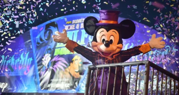 Mickey Mouse dazzles in a purple hat and striped suit, celebrating on stage as colorful confetti rains down during the Wine & Dine Half Marathon festivities at Disney World.