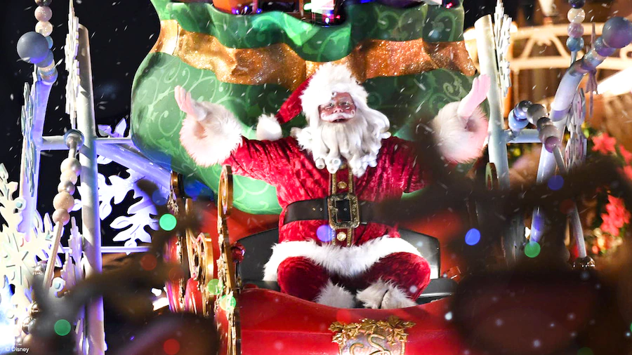 Santa Claus greets guests with a cheerful wave from his dazzling sleigh as he glides through the park’s nighttime holiday parade, surrounded by twinkling lights and magical snowfall.
