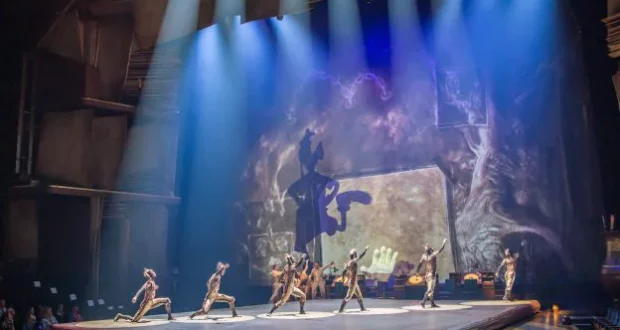 Cirque du Soleil performers twirl and leap in vibrant costumes across a luminous blue stage, surrounded by sweeping shadows and imaginative projections that bring the whimsical artistry of Disney’s Drawn to Life to life through breathtaking acrobatics and magical animation.