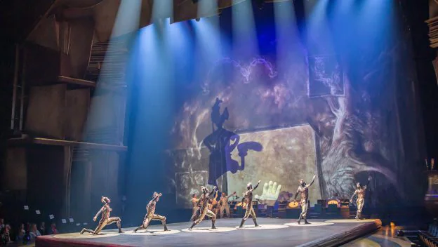 Cirque du Soleil performers twirl and leap in vibrant costumes across a luminous blue stage, surrounded by sweeping shadows and imaginative projections that bring the whimsical artistry of Disney’s Drawn to Life to life through breathtaking acrobatics and magical animation.