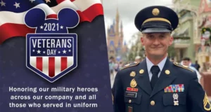 A proud veteran in uniform stands beside the vibrant 2021 Veterans Day Disney sign, celebrating military heroes and Disney Cast Members who serve, creating a special moment of tribute within the magic of the park.